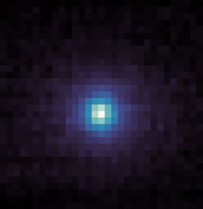 A square, pixelated image with a dark background. At the center is a roughly circular cluster of bright pixels, transitioning from white at the very center to light blue, then darker blue and purple as it spreads outward. The edges and corners of the image are mostly dark purple and black pixels.